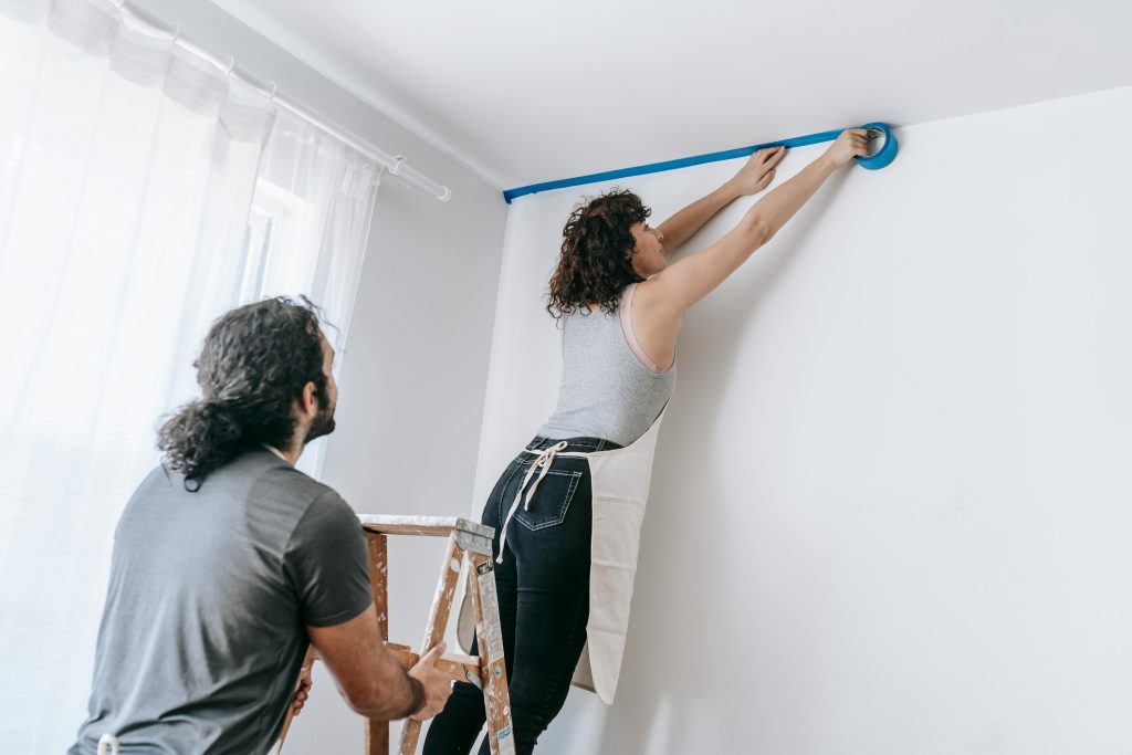 A man and woman painting a room together with blue paint, focused on their task and surrounded by painting supplies
