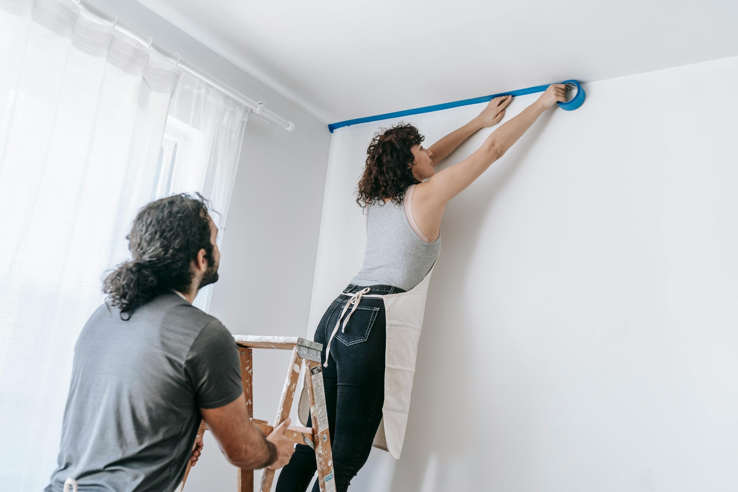 A man and woman painting a room together with blue paint, focused on their task and surrounded by painting supplies