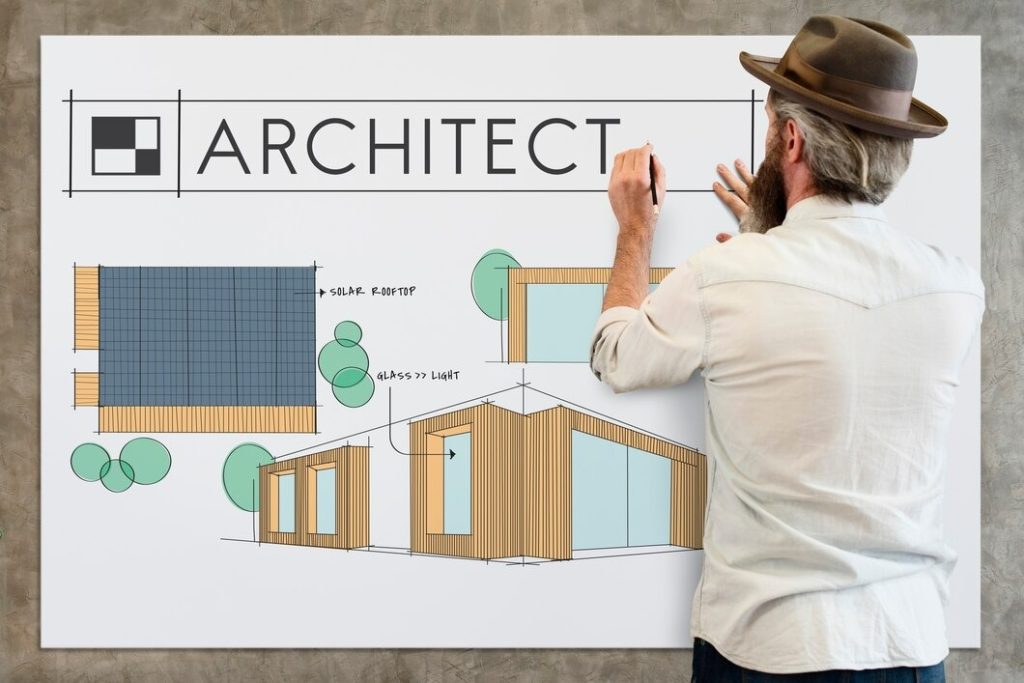 A man sketches a house on a whiteboard, focusing intently on the details of the drawing